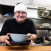 脂、増しときました！ラーメン店の店長が丼を持ってほほ笑むの写真