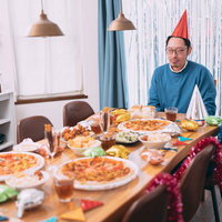 パーティーのはずが不正解の部屋でぼっち、赤い帽子をかぶって一人でピザを前にの写真