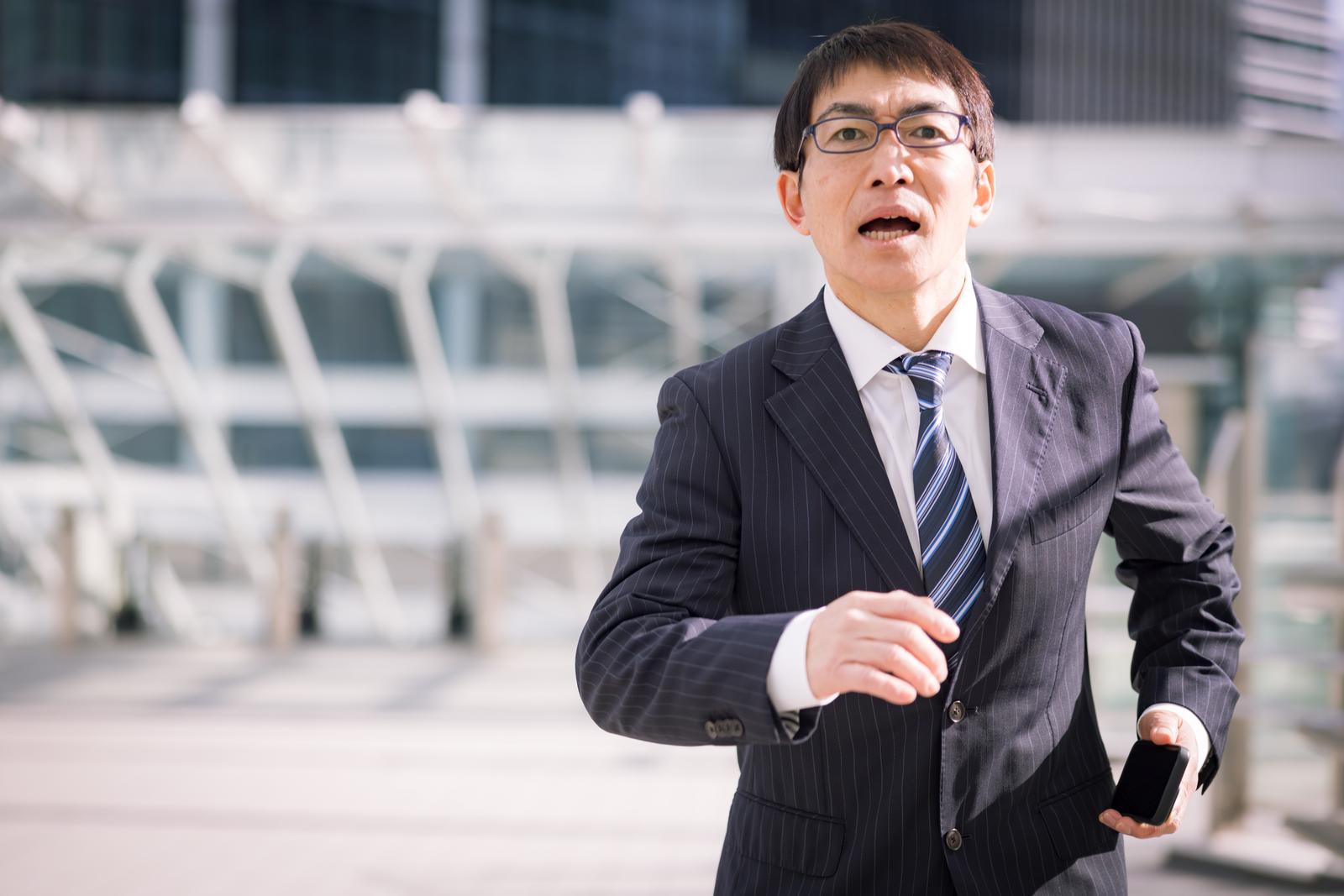 スーツを着た男性がスマートフォンを持ちながら走っている［モデル：ガーミー］