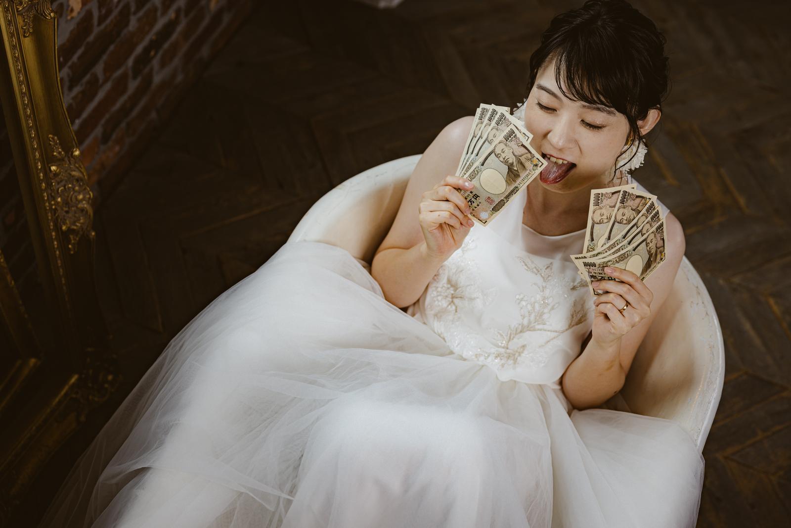 ウェディングドレス姿の花嫁が札束を持って喜ぶ［モデル：たけべともこ］