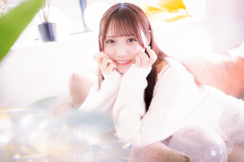 両手を頬に添えてにっこり笑う女性、白いニット姿でソファーでリラックス