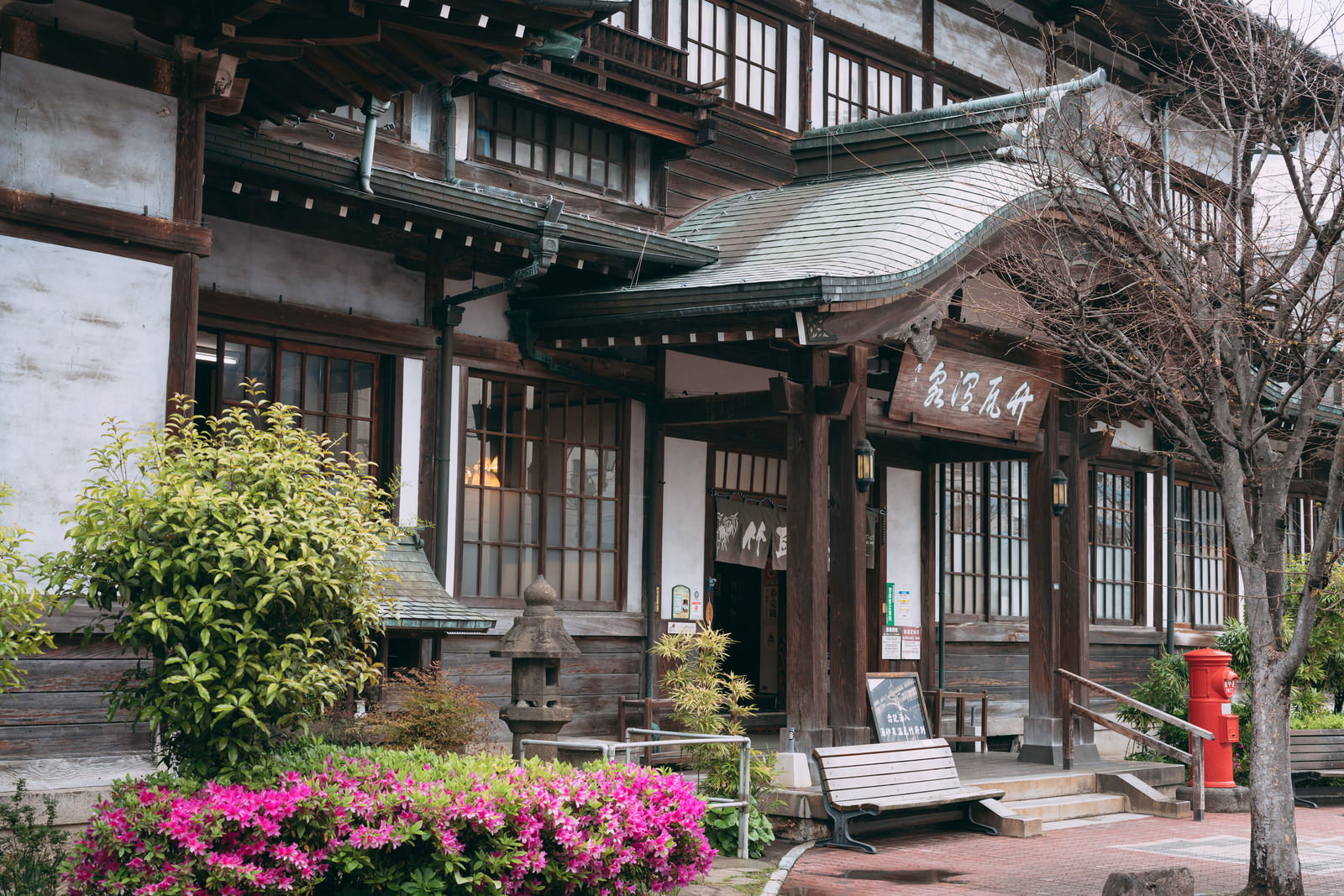 木造の伝統的な建物の竹瓦温泉の外観、緑の植栽とピンクの花が飾られた入口