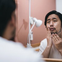 洗面所で無精髭が気になる男性のモーニングルーティングの写真