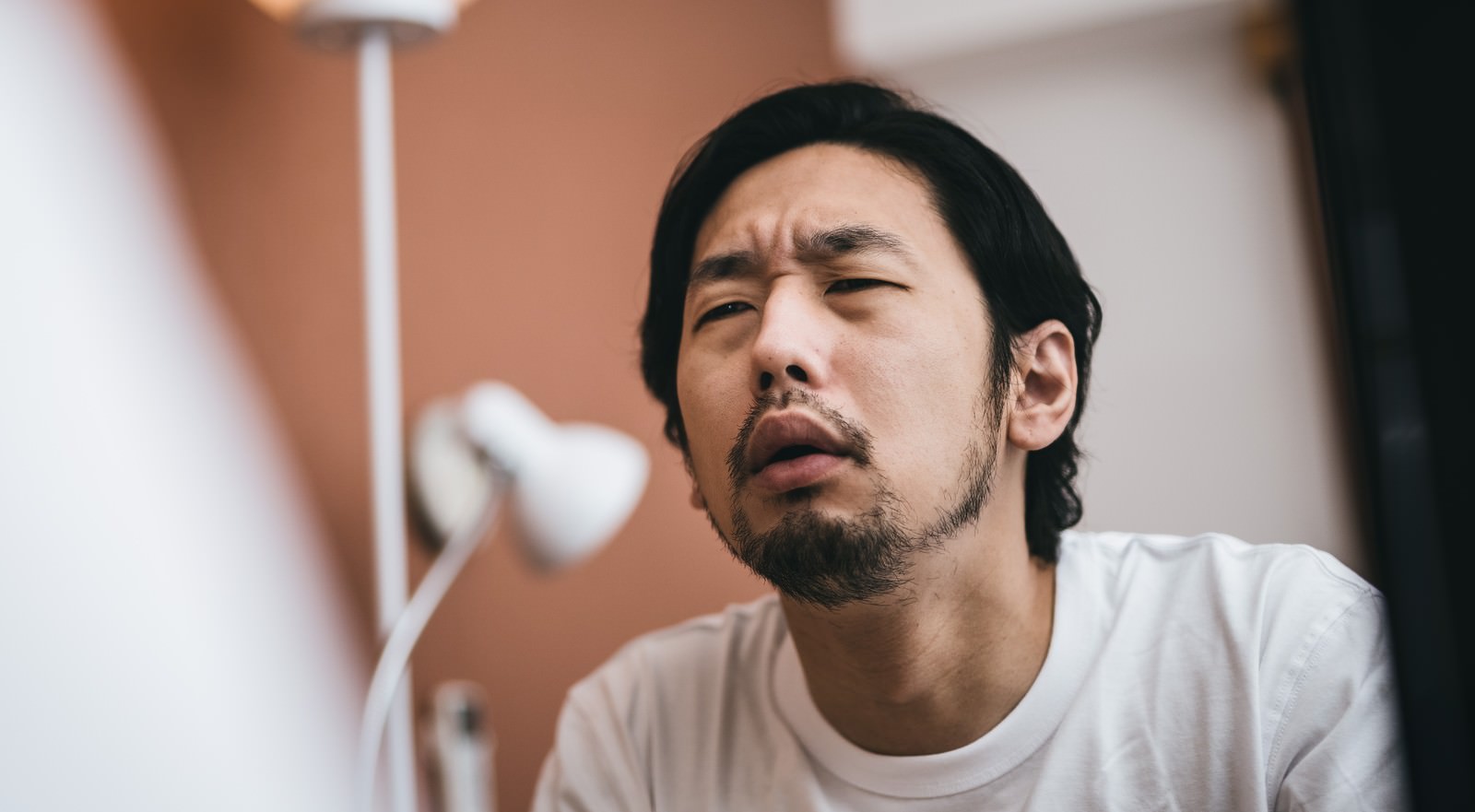 無精髭を生やした男性が眉間にしわを寄せて驚いた表情を見せている［モデル：大川竜弥］