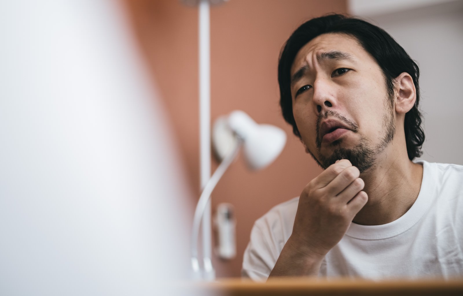 洗面台で毛抜きを使ってあご髭を処理している男性［モデル：大川竜弥］