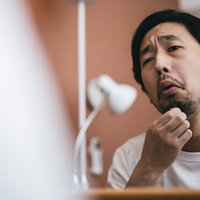 あご髭に1本だけある白髪を毛抜きで処理する男性の写真