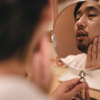 手鏡で肌のコンディションと伸びた髭をチェックする男性の朝の身だしなみの写真