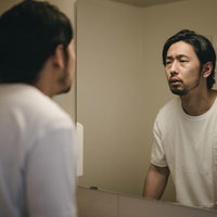 寝起きの顔はむくみがち、無精髭の男性が鏡を見つめるの写真