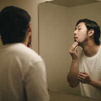 洗面台の鏡で髭の伸び具合を確認する男性の朝の身支度の写真