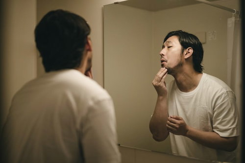 洗面台の鏡で髭の伸び具合を確認する男性の朝の身支度