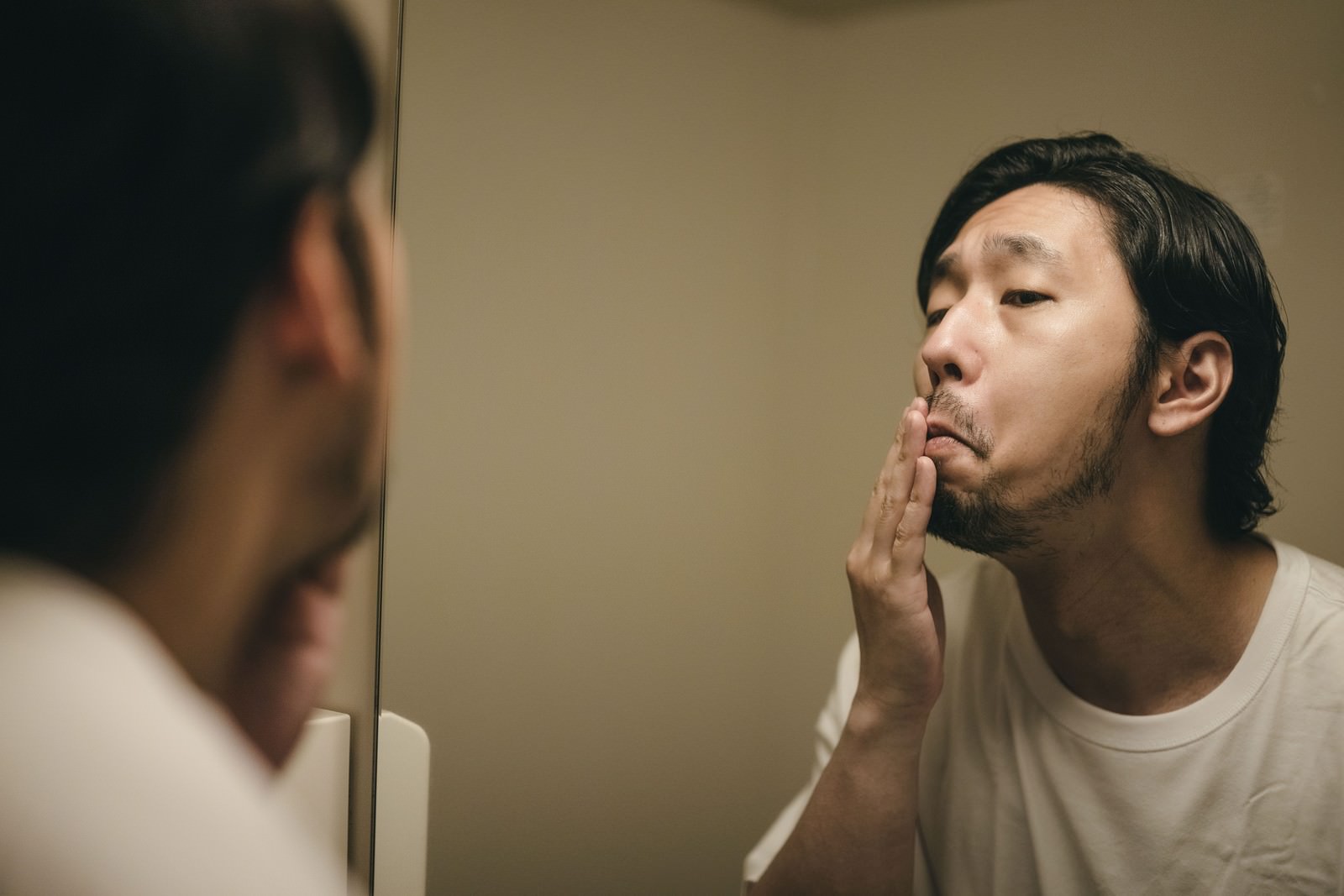 洗面所の鏡の前で髭の伸び具合を確認している男性［モデル：大川竜弥］