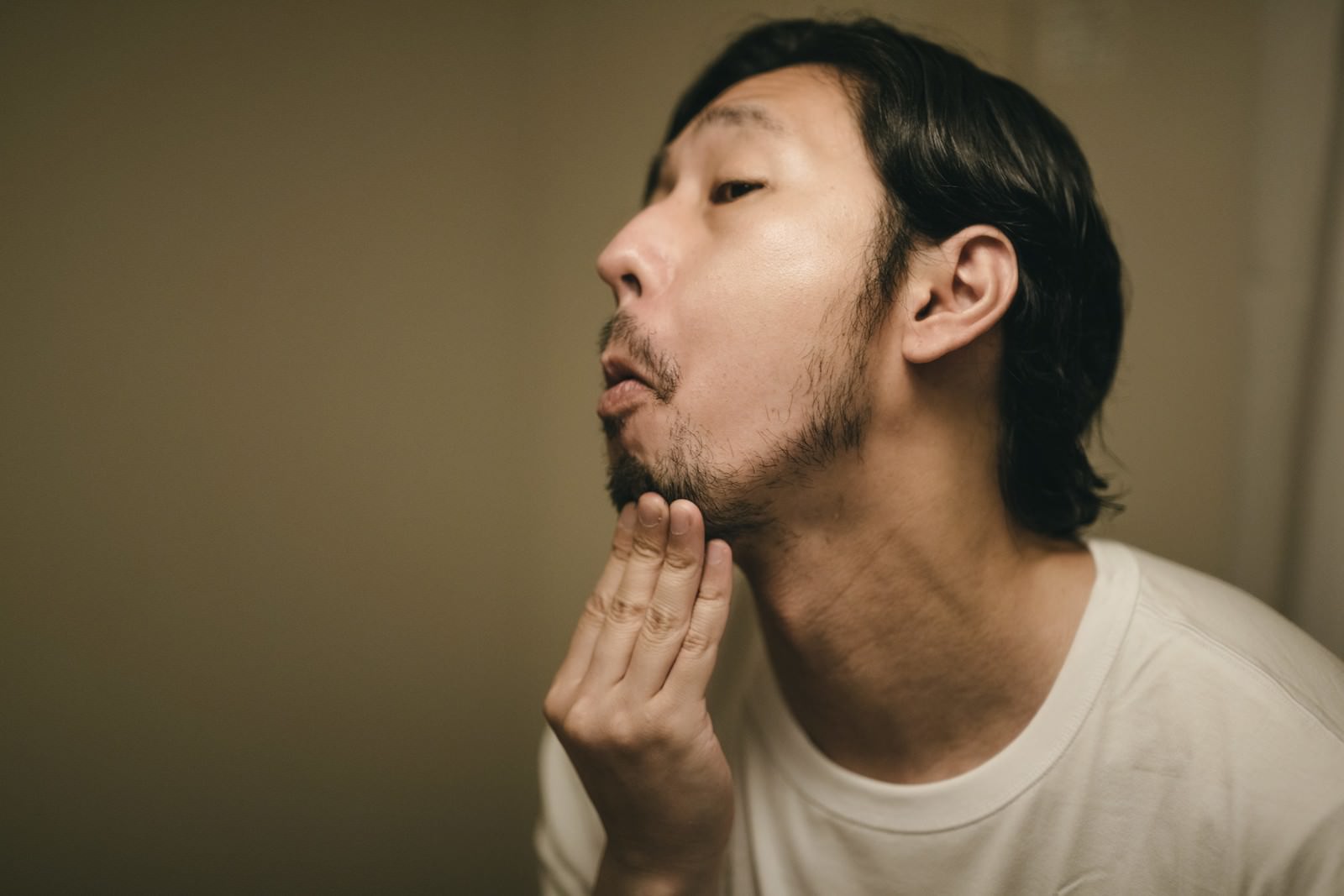 白いTシャツを着た男性が顎に手を当てて髭の伸び具合を確認している［モデル：大川竜弥］