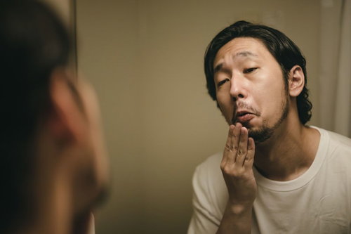 デスマ中は髭が伸びるの早いなぁ、洗面台で無精髭を確認する男性