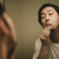 髭を整えながら顔を歪める髭面の男性の朝のスキンケアルーティンの写真