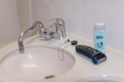 洗面台に無造作に置かれた電動シェーバーとシェービングクリーム