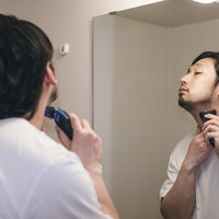 洗面台の鏡の前でシェービングフォームを塗って髭剃り中の男性の写真
