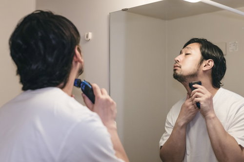 洗面台の鏡の前でシェービングフォームを塗って髭剃り中の男性