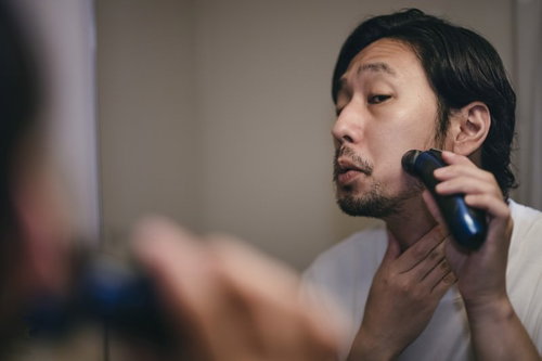 もみあげから髭にかけてシェーバーでシェービングする男性