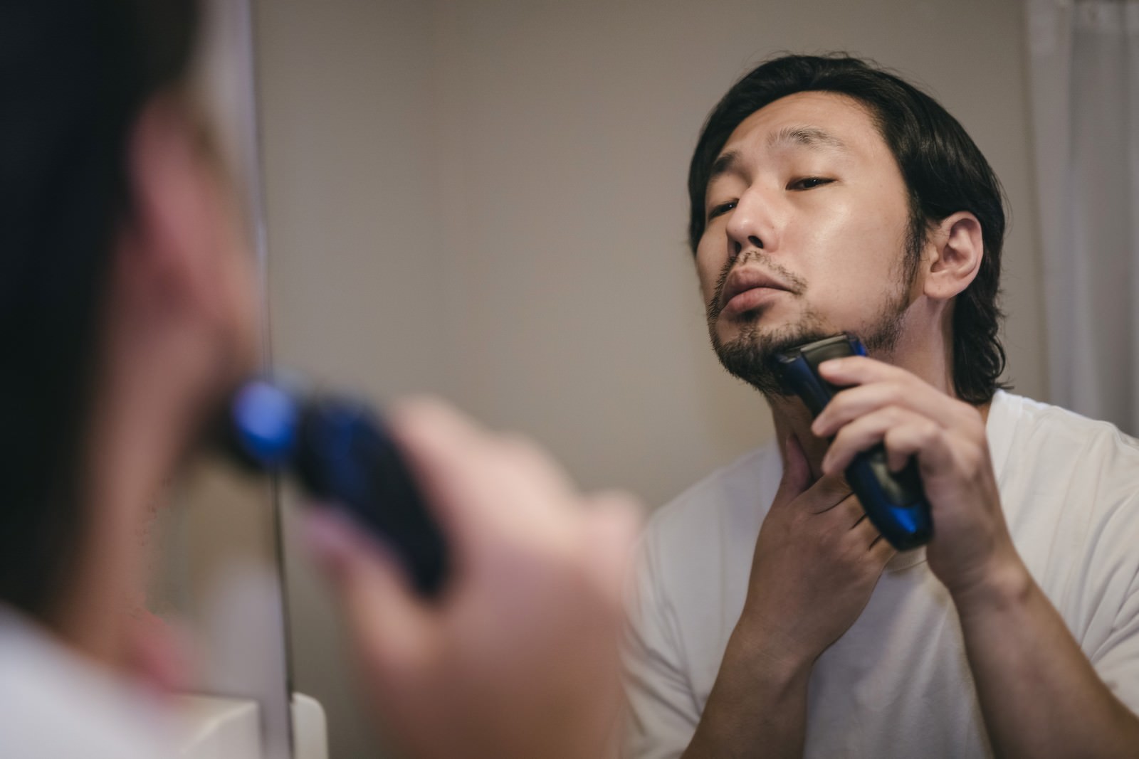 洗面所の鏡の前で電動シェーバーを使って髭を剃っている男性［モデル：大川竜弥］