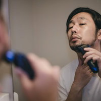伸びた無精髭を電動シェーバーで剃る男性の身だしなみの写真