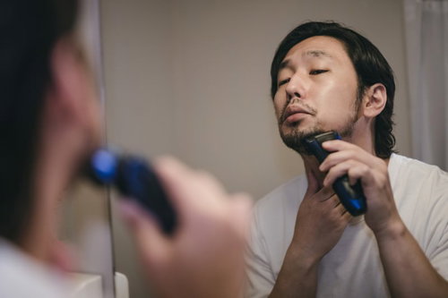 伸びた無精髭を電動シェーバーで剃る男性の身だしなみ