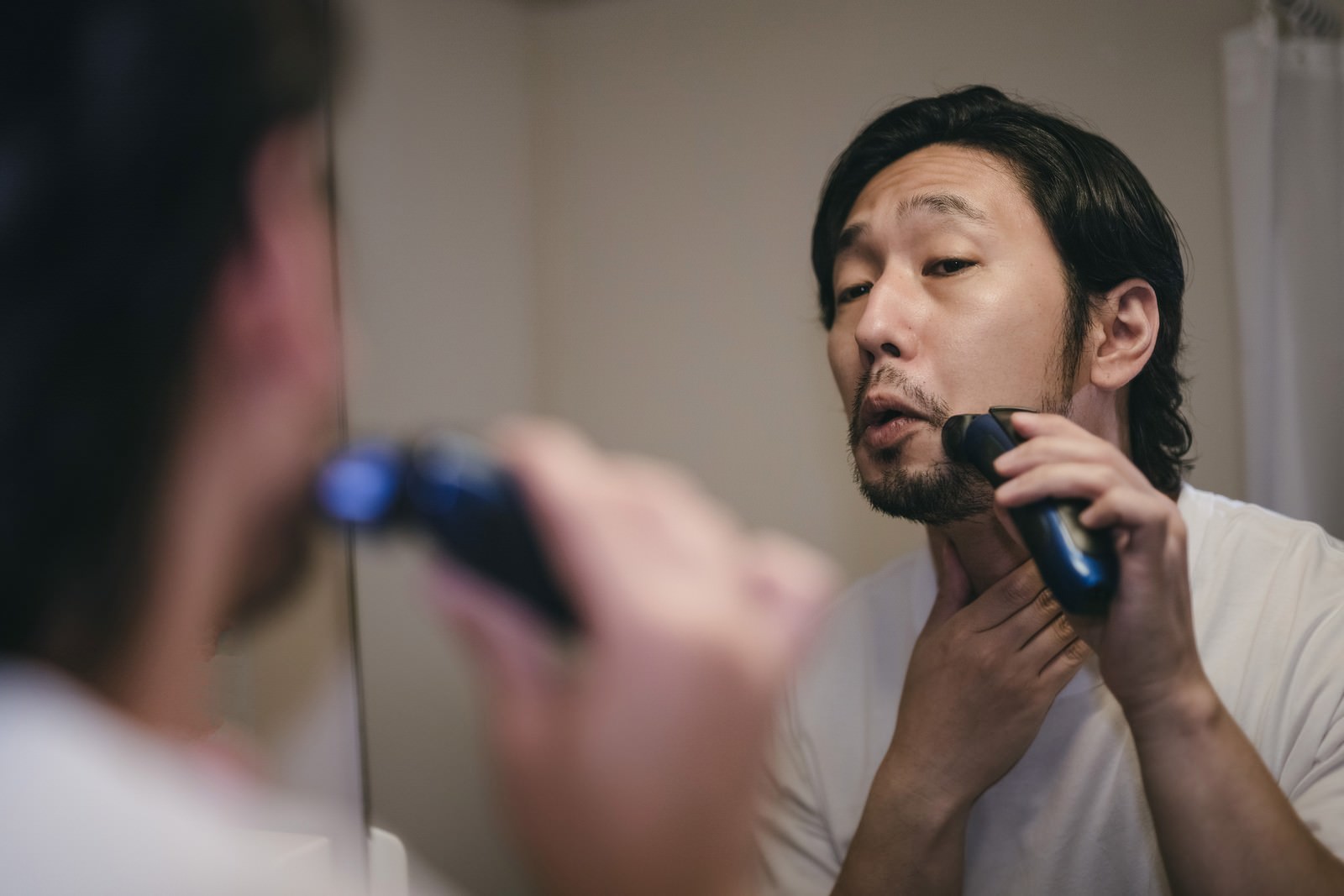 長い髭が電気シェーバーに絡まりながら髭剃りをする男性［モデル：大川竜弥］