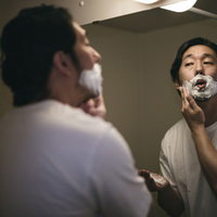 洗面所の鏡の前でシェービングクリームを口の周りに塗る男性の写真