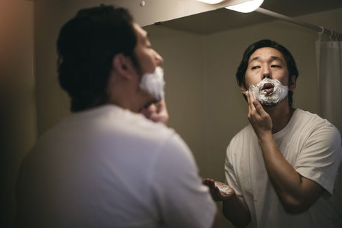 洗面所の鏡の前でシェービングクリームを口の周りに塗る男性