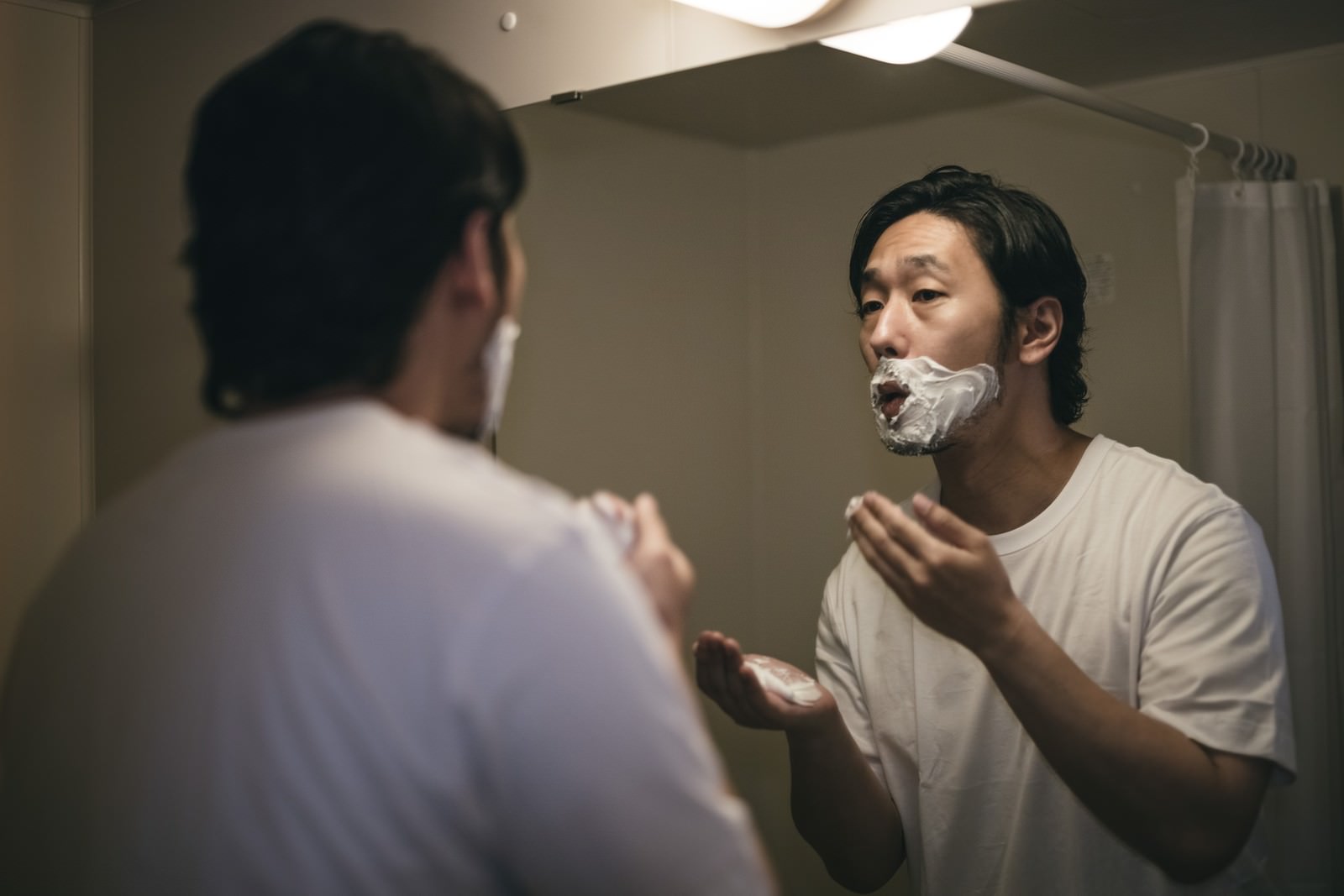 洗面所の鏡の前でシェービングクリームを口元に塗る男性［モデル：大川竜弥］