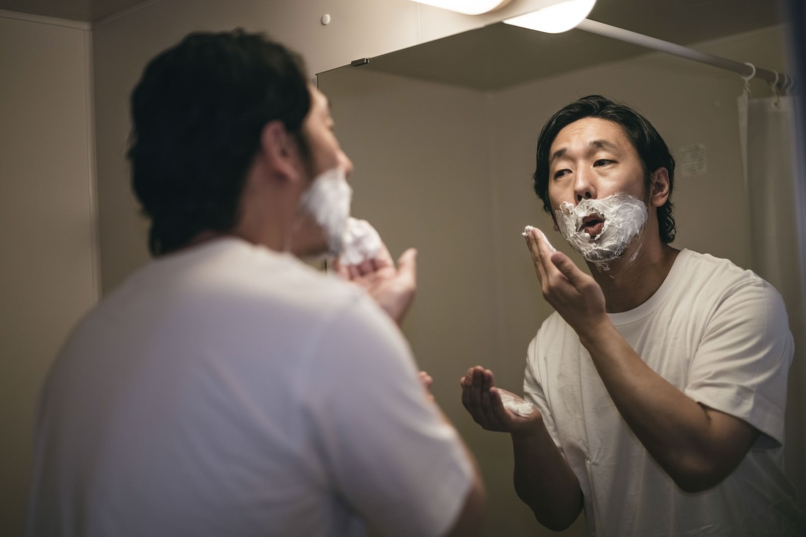 鏡の前でシェービングクリームを顔に塗る男性［モデル：大川竜弥］