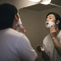 洗面台の鏡の前でシェービング用の泡を塗り込む男性の写真