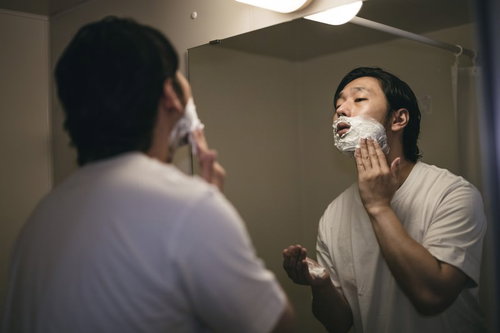 洗面台の鏡の前でシェービング用の泡を塗り込む男性