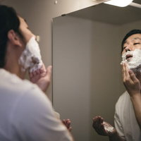 洗面所で髭剃り用の泡を顔に塗る男性の写真