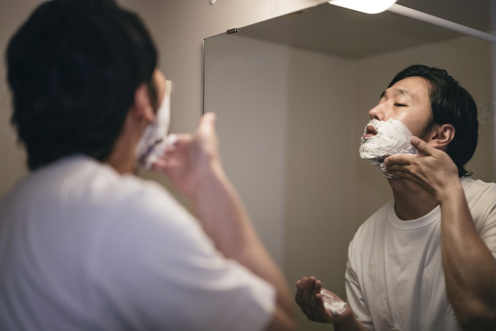 洗面台の鏡の前でシェービングクリームを顔に塗る男性［モデル：大川竜弥］