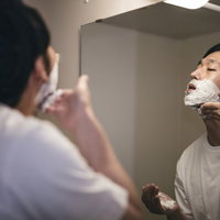 洗面台でシェービング剤の泡を入念に塗り込む男性の写真