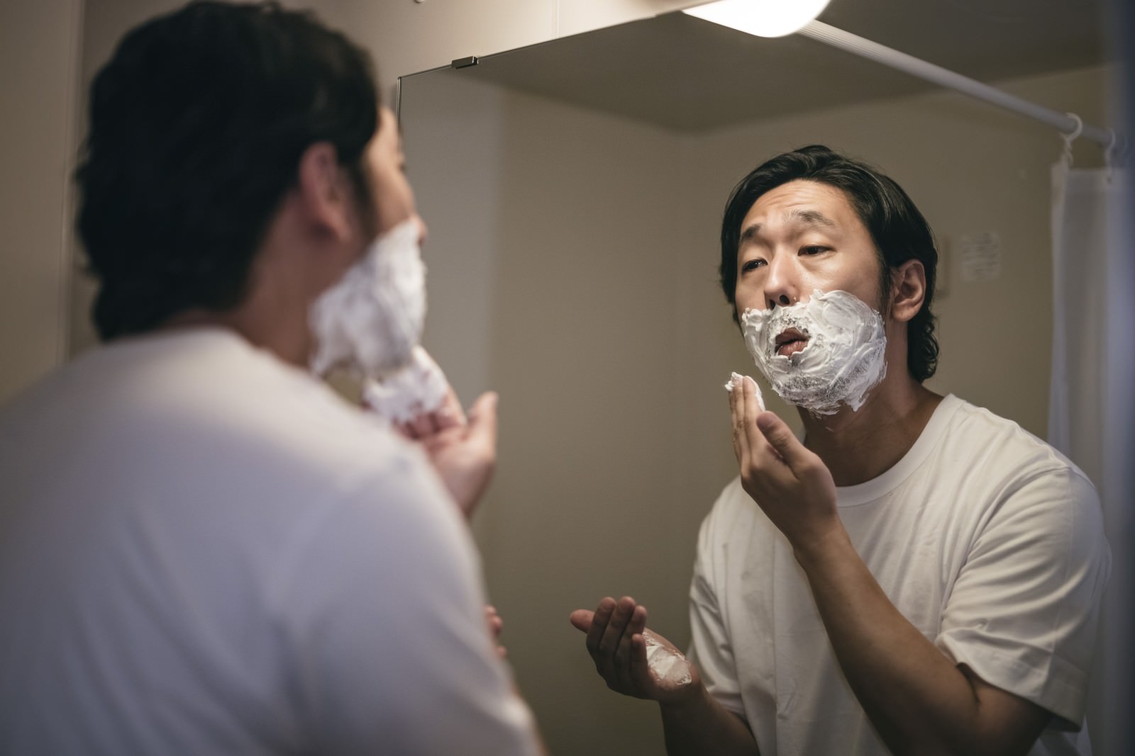 洗面所の鏡の前でシェービング剤を顔に塗った男性［モデル：大川竜弥］