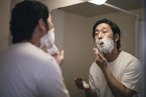 口周りにシェービング剤の泡を塗った髭剃りをする男性
