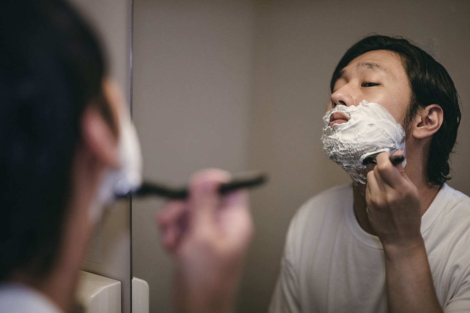 洗面所の鏡の前でシェービングクリームを塗りカミソリで髭を剃る男性［モデル：大川竜弥］