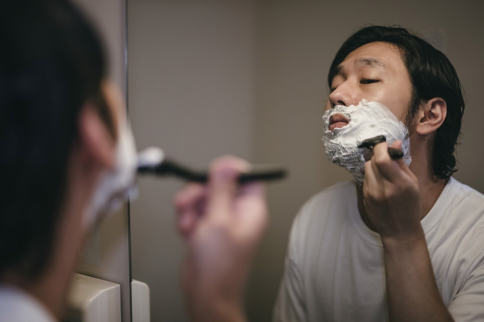 鏡を見ながらシェービング剤の泡をつけてカミソリで髭を剃る男性［モデル：大川竜弥］