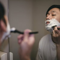 鏡を見て白いシェービング剤の泡を使いながら慎重にシェービングする男性の写真