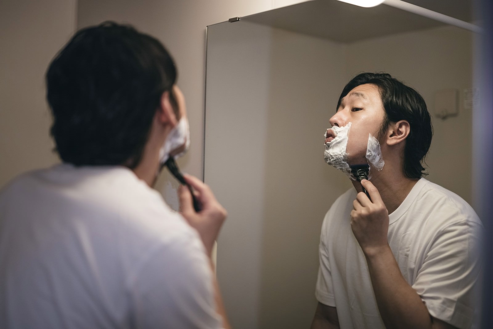 洗面台の鏡の前でシェービング剤を使って髭剃りをしている男性［モデル：大川竜弥］