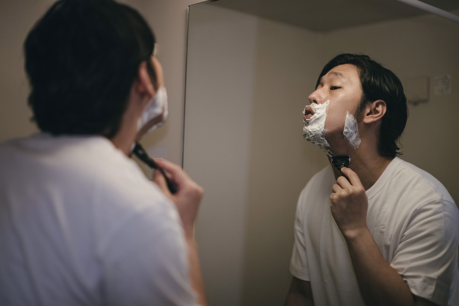 洗面台の鏡の前でシェービングフォームを使って髭剃りをする男性［モデル：大川竜弥］
