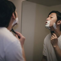 頬から首元までシェーバーを走らせてシェービングする男性の写真