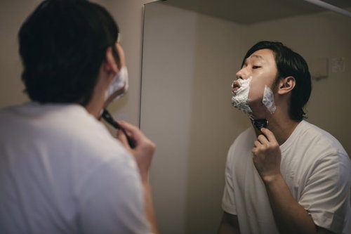 頬から首元までシェーバーを走らせてシェービングする男性