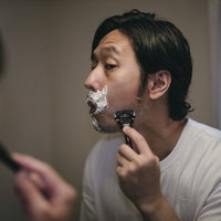 洗面所でカミソリを使って髭剃りをする男性の写真