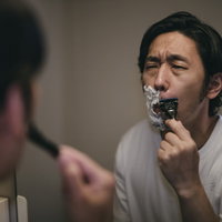 白いシェービング剤の泡をつけてしかめっ面して鼻下を剃る男性の写真