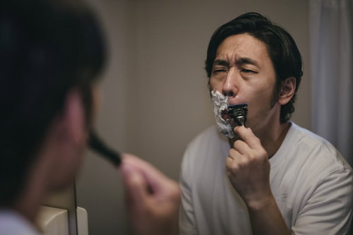 白いシェービング剤の泡をつけてしかめっ面して鼻下を剃る男性