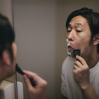 鏡を見ながらカミソリで髭を剃る男性のグルーミングの写真
