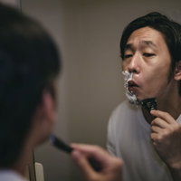 洗面所の鏡の前で左側面をシェーバーで剃り上げる男性の写真