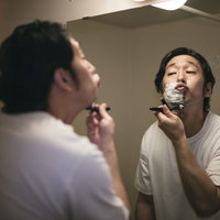 洗面所で白い泡をつけてカミソリで髭を剃る男性の写真